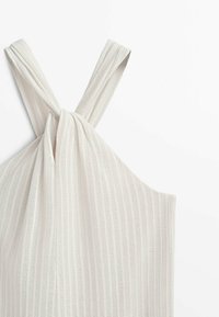 Haut halter ivoire clair avec un motif côtelé texturé. Présente des bretelles torsadées et une silhouette ample et fluide. Confectionné dans un tissu doux et respirant.