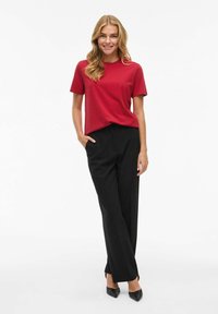 T-shirt rosso a maniche corte abbinato a pantaloni neri a vita alta e tacchi a punta neri. L'outfit presenta una vestibilità classica e una texture liscia.