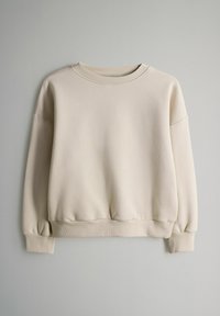 Beige crewneck collegepaita, jossa on ribbikujat hihansuissa ja helmassa, esiteltynä litteänä harmaata taustaa vasten.