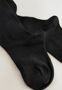 Chaussettes en coton noires à texture lisse, avec un design côtelé à la cheville et un bout arrondi. Simple et de couleur unie.