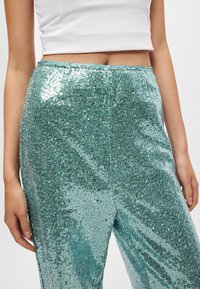 Τουρκουάζ παντελόνι με παγιέτες διαθέτει ψηλή μέση με λείο υφή, αντανακλώντας το φως με λαμπερά στοιχεία σε όλη την επιφάνειά του.