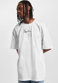 White cotton t-shirt with a loose fit, round neck, and short sleeves. Features a black embroidered logo on the front.
