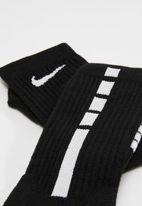 Mustad ribadega valmistatud mustad sokid, mille külgedel on valge Nike logo ning horisontaalsed ja vertikaalsed valged triibud.