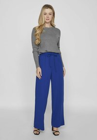 Suéter gris de manga larga combinado con pantalones azules de pierna ancha que presentan un cinturón para atar. Los pantalones tienen una textura suave y caen elegantemente.