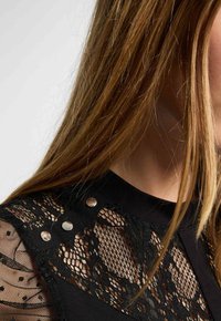 Top nero con maniche in pizzo e motivi floreali e pois, arricchito da bottoni a scatto argentati sulla spalla.