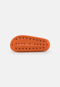 Semelle de chaussure en caoutchouc orange présentant un motif zigzag texturé et des trous de ventilation, avec une forme effilée et une finition lisse.