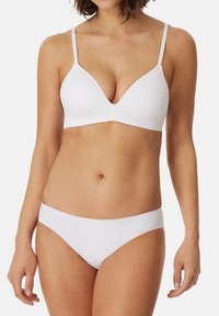 Bralette bianco e slip coordinati, entrambi realizzati in tessuto morbido. Il bralette presenta una scollatura profonda e spalline regolabili. Design minimale.