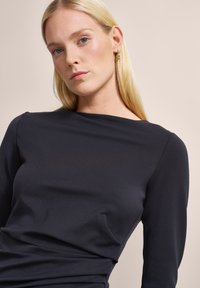 Schwarzes Langarmoberteil mit rundem Ausschnitt, aus glattem Stoff gefertigt. Verfügt über ein minimalistisches Design und eine figurnahe Silhouette.