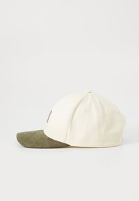 Beige baseball cap with six panels and small ventilation holes, featuring an olive-green suede curved brim, shown from the side on a white background.