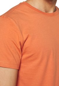 Camiseta de manga corta en algodón naranja, con un clásico cuello redondo, textura suave y costuras mínimas para un diseño limpio.