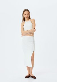 Weißes, geripptes Zweiteiler-Outfit mit einem Halterneck-Top und einem langen Rock mit seitlichem Schlitz, kombiniert mit braunen, gemusterten Ballerinas.