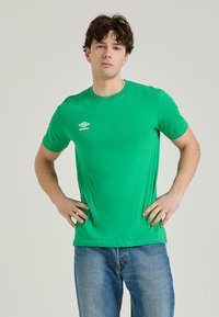 T-shirt verde a maniche corte realizzato in tessuto morbido, con scollatura rotonda e logo bianco sul lato sinistro del petto, abbinato a jeans blu.