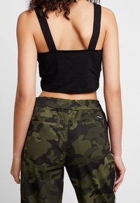 Zwarte cropped top met brede banden, gecombineerd met groene camouflage cargobroek met een elastische tailleband en achterzakken.