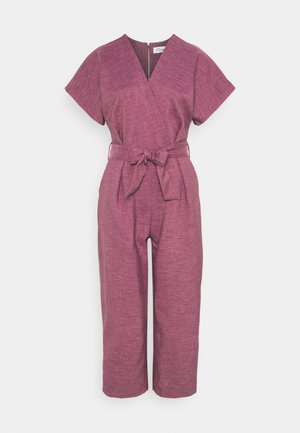 Kortærmet mauve buksedragt med V-hals, vide ben og et bundet bælte i taljen, vist på en ensfarvet baggrund.