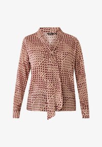 Blusa a maniche lunghe beige con un motivo geometrico rosso, dotata di chiusura a fiocco sul collo e di una vestibilità morbida. Tessuto dalla texture liscia.