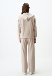 Completo da sudore beige coordinato, composto da una felpa con cappuccio e pantaloni larghi, realizzato in tessuto morbido con una superficie testurizzata.