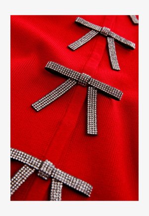 Sarkans adīts apģērbs ar trim metāla izdomātiem rhinestone rotātiem lokiem, kas demonstrē gludu tekstūru un pieguļošu dizainu.