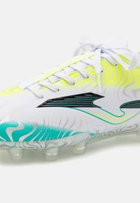 Scarpe da calcio bianche con motivi a onda gialli e turchesi, tomaia sintetica, dettagli neri e tacchetti trasparenti sulla suola. I lacci sono bianchi.