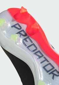 Semelle de crampons de football noire avec des sections transparentes, des crampons rouges et verts, et la marque "PREDATOR" en lettres majuscules au centre.