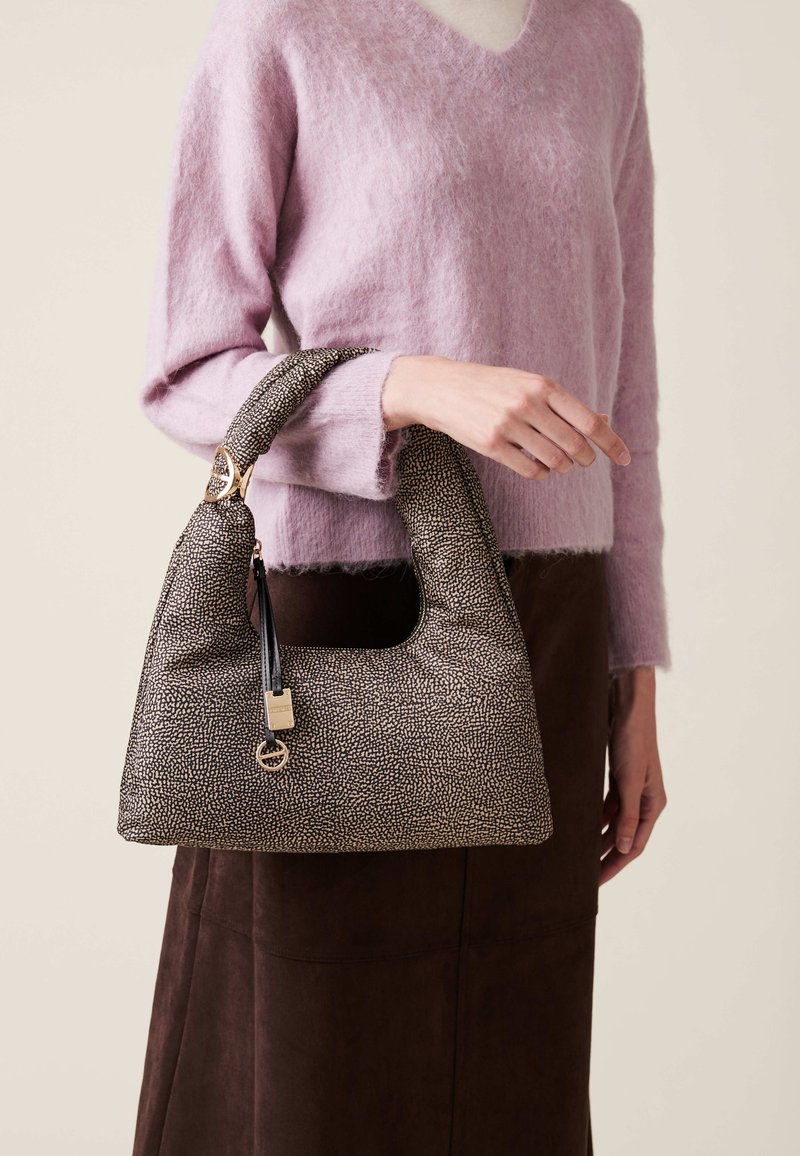 Brown speckled leather handbag with a curved handle, gold hardware, and a black strap detail, paired with a soft lavender sweater and brown skirt.