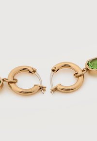 Χρυσά σκουλαρίκια κρίκοι με κούμπωμα και συνδεδεμένα πράσινα πολύεδρα πετράδια σε λευκό φόντο.