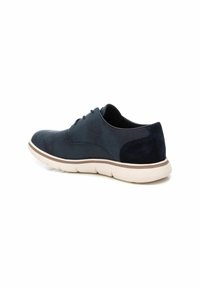 Zapato de ante azul marino con cordones, con un empeine suave, cuello acolchado, suela de goma blanca y sutiles detalles de costura.