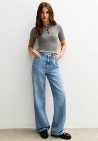 Grau gestreiftes Polohemd mit kurzen Ärmeln und schwarzen Knöpfen, kombiniert mit weit geschnittenen hellblauen Jeans und schwarzen flachen Schuhen.