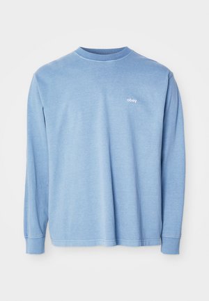 Jasnoniebieska koszula z długim rękawem, wykonana z miękkiego materiału, z okrągłym dekoltem i małym białym logo "obey" na piersi.