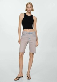 Crni crop top s prilagođenim dizajnom uparen s svijetlopinkastim traper Bermuda šortsevima, koji imaju razderani rub i svijetloplave šavove.