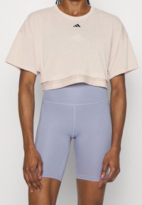 Różowy krótki t-shirt z okrągłym dekoltem i małym czarnym logo Adidas, w połączeniu z wysokim stanem jasnofioletowych szortów rowerowych o gładkiej fakturze.