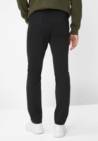 Pantaloni neri slim-fit realizzati in tessuto liscio, dotati di due tasche posteriori e una cintura pulita, abbinati a sneakers bianche.