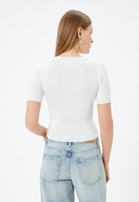 Witte ribbel top met korte mouwen en een ronde halslijn, gecombineerd met lichtblauwe high-waisted jeans met een vervaagde wassing en twee achterzakken.