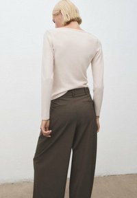 Maglione fitted beige chiaro a maniche lunghe con scollo ampio, abbinato a pantaloni a gamba larga marrone scuro con tasche posteriori.