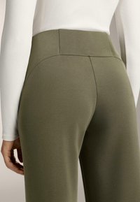 Olajzöld, magas derekú nadrág sima, rugalmas anyagból. Görbült varrások találhatók a zsebek mentén, és testhezálló fazonú.