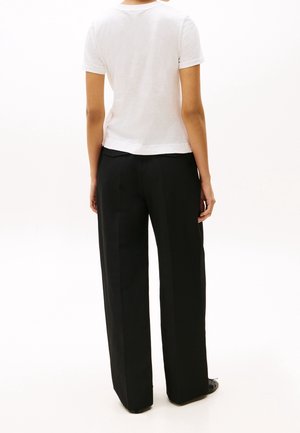 Person standing facing away wearing a white short-sleeve shirt and loose black wide-leg pants on a white background.