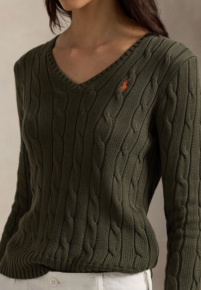 Vihreä neulottu V-kaula-aukolla varustettu neulepaita, jossa on palmikkoneulekuvio ja oranssilla vasemmalla puolella oleva logo. Resoroidut hihansuut ja helma.