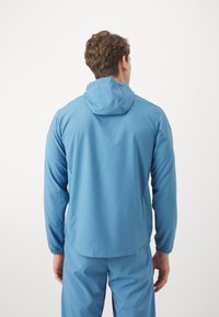 Blå letvægts hættetrøje med en glat tekstur og elastiske manchetter, der har en bagsømsdetalje og et afslappet fit design.
