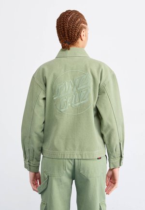 Vihreä farkkutakki, jossa on kirjailtu "SANTA CRUZ" -logo selässä, kaulus ja napitettu hihansuut. Mallilla on päällään matching cargo-housut.