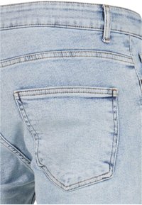 Jean en denim bleu clair montrant la poche arrière et la boucle de ceinture avec des détails de couture visibles.