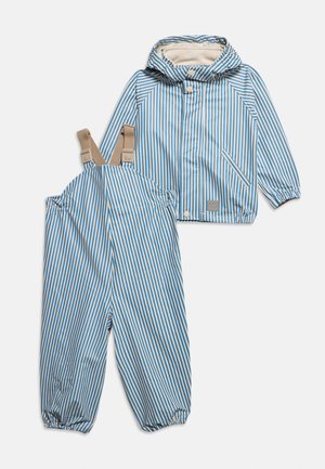 Veste imperméable pour enfants à rayures bleues et blanches avec capuche, accompagnée d'une salopette imperméable assortie avec des bretelles ajustables beiges.