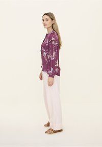 Pflaumenblumen-Bluse mit langen Puffärmeln, kombiniert mit hellrosa weit geschnittenen Hosen und braunen Sandalen mit goldener Schnalle.