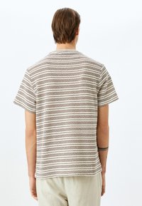 Camisa de manga corta hecha de tejido texturizado, con franjas horizontales en beige y marrón que alternan. Diseño de cuello redondo simple.