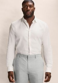 Weißes Langarmhemd mit strukturiertem Finish, button-down Kragen und grauen maßgeschneiderten Hosen. Glattes Material, taillierte Passform, neutrale Farbe.