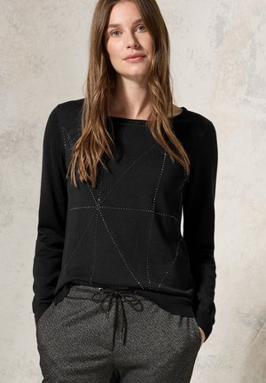 Pull noir à manches longues avec un motif géométrique créé par des accents en points, associé à un pantalon en pied-de-poule gris avec une taille élastique.