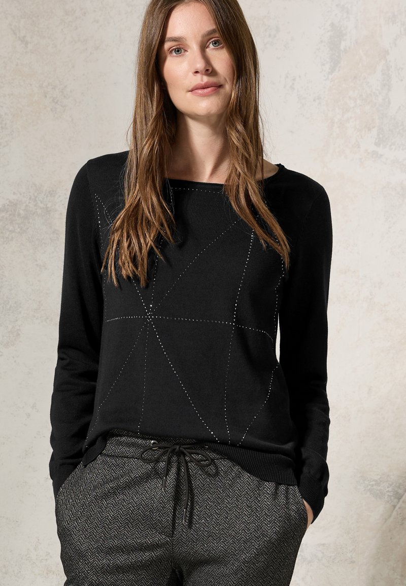 Maglione nero a maniche lunghe con un motivo geometrico creato da accenti a pois, abbinato a pantaloni houndstooth grigi con cintura elastica.