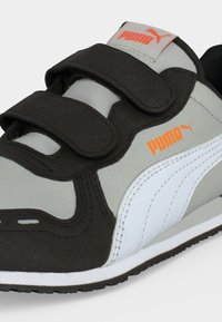 Scarpa da ginnastica Puma grigia e nera per bambini con due strisce in velcro nere e loghi Puma arancioni sulla linguetta e sul lato.