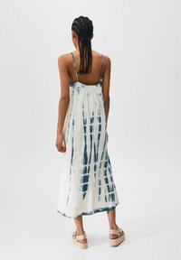 Abito midi in tessuto leggero caratterizzato da un motivo tie-dye blu e bianco, con spalline sottili e una vestibilità ampia che cade sotto il ginocchio.