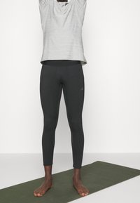 Camiseta gris de manga corta que absorbe la humedad, con un cuello redondeado, combinada con leggings negros ajustados. Ambas prendas están hechas de tela elástica.