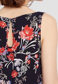 Tessuto a fantasia floreale in blu navy, con fiori rossi e blu. Sul retro è visibile un dettaglio con scollo a goccia, che aggiunge interesse al design.