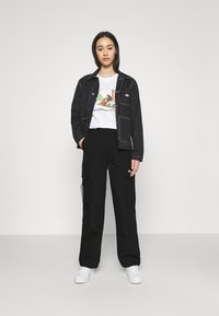 Zwarte denim jack met witte stiksels, grafisch wit T-shirt, zwarte cargobroek en witte sneakers. Eenvoudige, functionele ontwerpelementen.